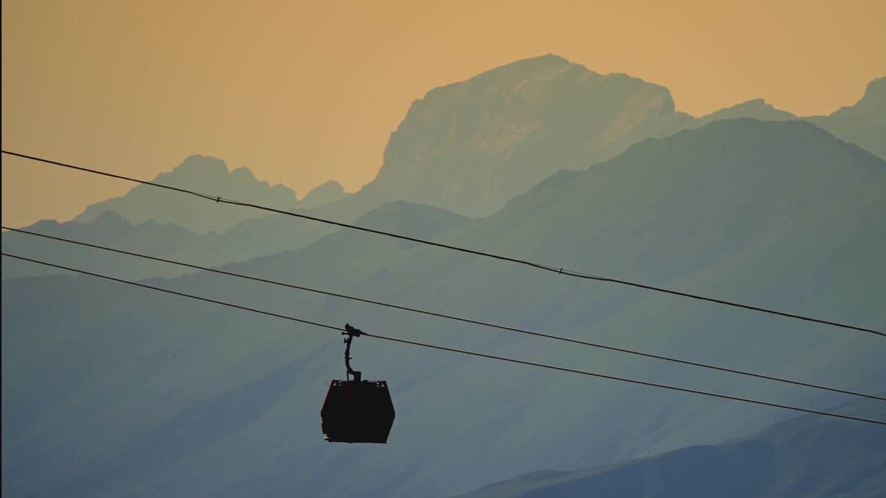 Silhouette di funivia che si muove attraverso montagne nebbiose al tramonto