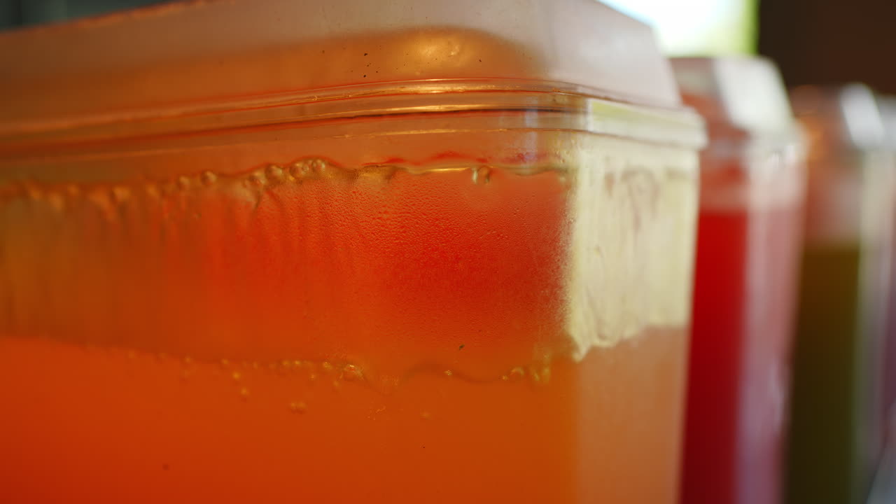 Distributore di succo d'arancia con contenitori colorati sullo sfondo.
