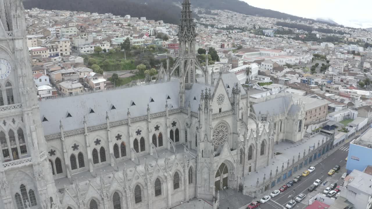 Drone shot of La Basilica del Voto Nacional located in the city of Quito, Ecuador during quarantine. Also, houses near the basilica and few cars parked on the streets. Pichincha mountain on the back.