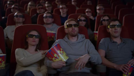 young people sitting in movie theater watching 3d movie and eating popcorn