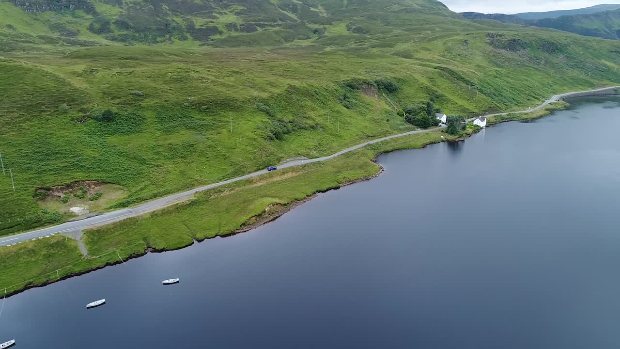 a lonely car is driving very close to the lake in the scottish isle of skye filmed with a drone