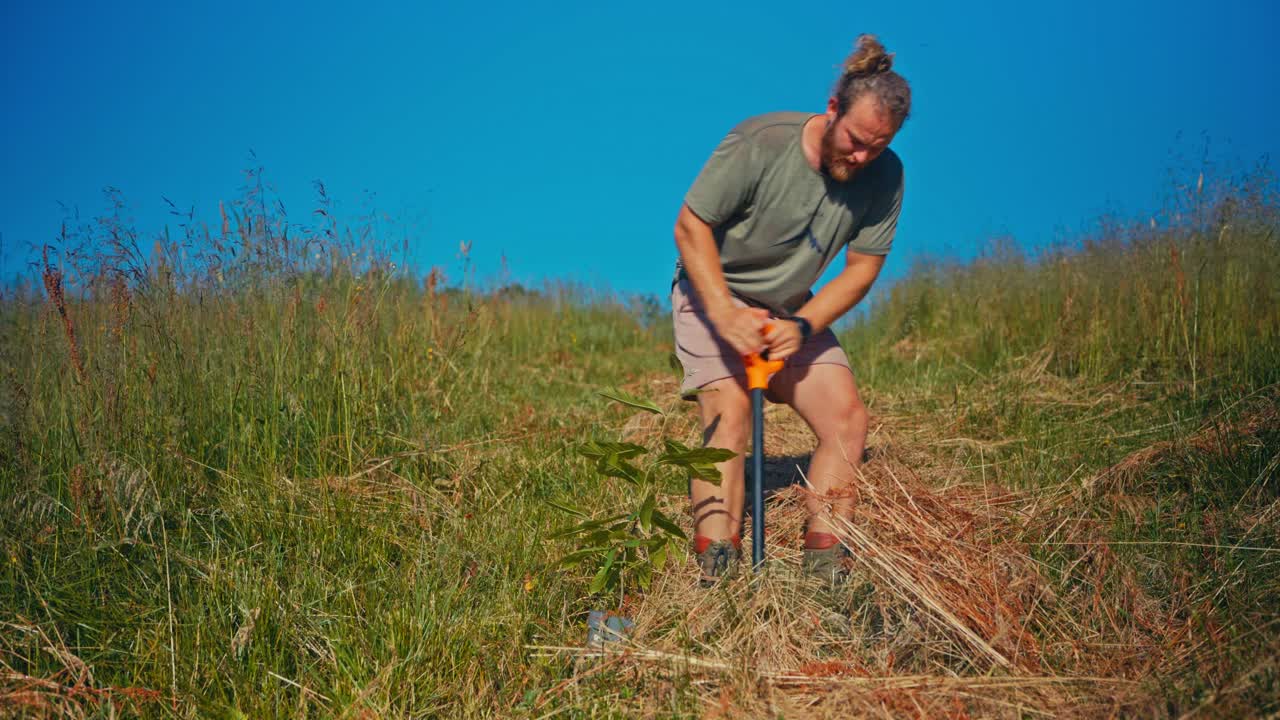 Um homem está envolvido em tarefas agrícolas, usando uma pá para revolver a terra em uma encosta gramada - Plano médio