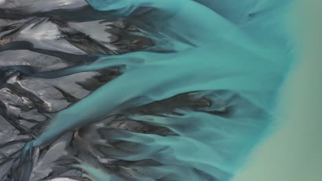 turquoise glacial braided river streams transition and flow into massive lake pukaki, top down aerial, new zealand