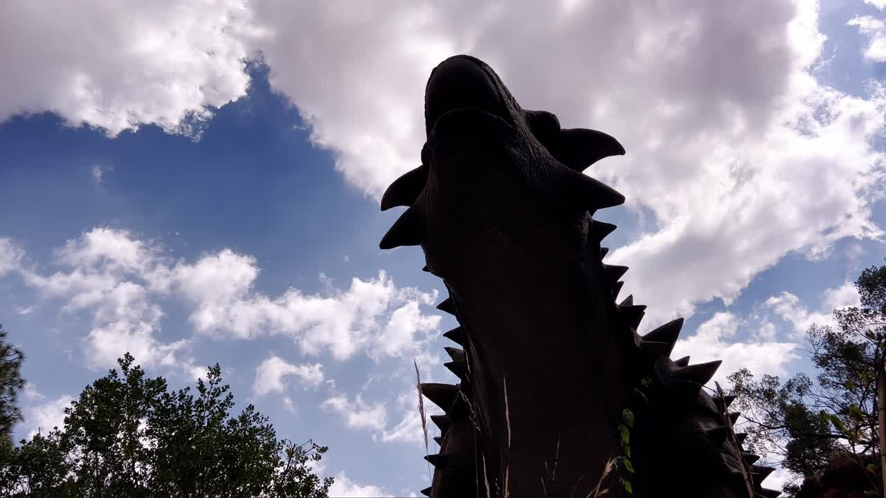 Contour of dinosaur stegosaurus statue against blue cloudy sky in amusement park, underside view