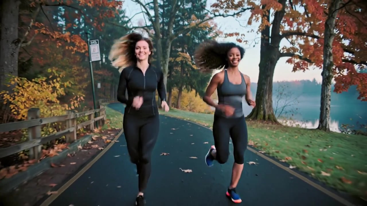 Due donne che fanno jogging su un sentiero del lago, in una fresca e motivante mattina d'autunno, indossano una giacca nera e una canottiera grigia.