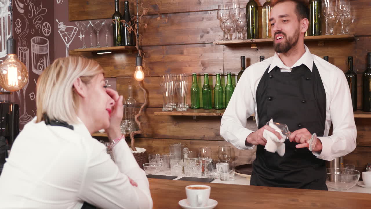 Bartender wiping glass while talking to a customer in a bar