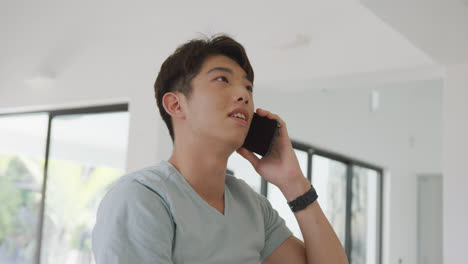 asian male teenager talking on smartphone and smiling in living room