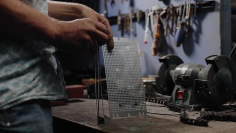 Cinematic-footage-of-old-fashioned-80s-styled-mechanic-handling-some-perforated-metal-on-his-workbench-in-his-garage