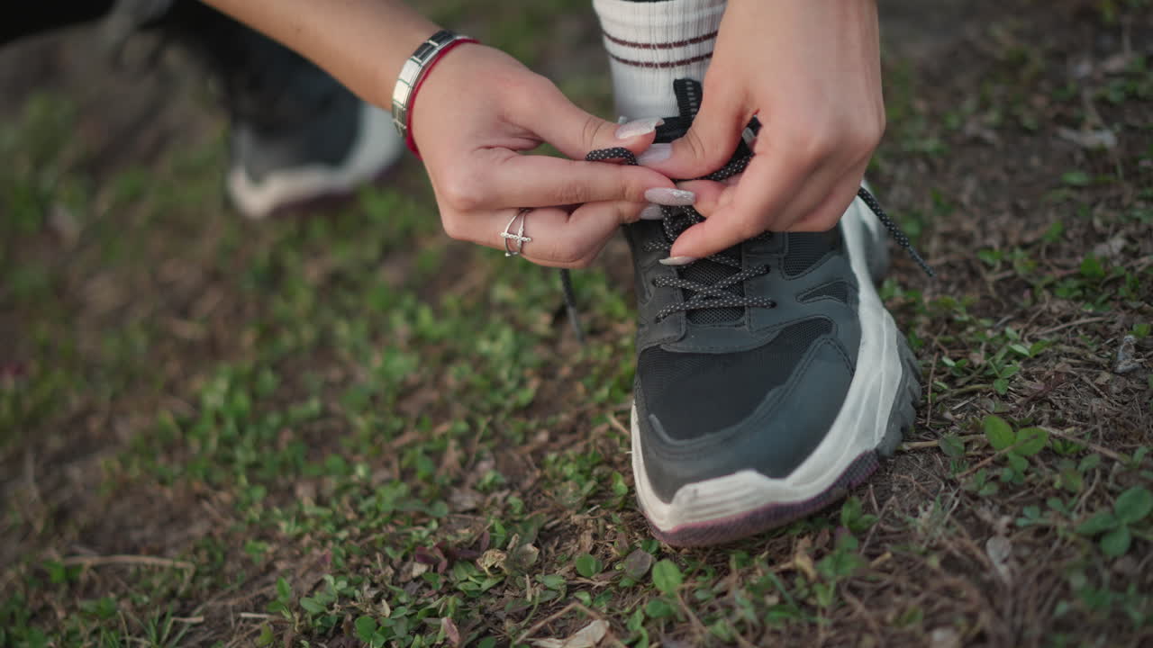 Primo piano di mani che allacciano le scarpe sull'erba, runner si prepara per la corsa mattutina con lacci allacciati e orologio, vista dettagliata di mani che legano i lacci delle scarpe sull'erba prima di iniziare l'allenamento mattutino