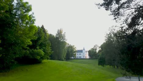 aerial drone flying through a national geographic yellow square and gliding over grassy green fields in a forest and ascends to reveal a large and majestic alatskivi castle during summet sunshine time