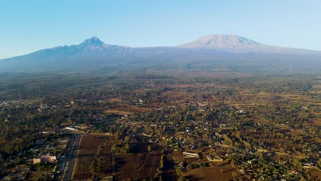 Sunrise--Kenya-landscape-with-a-village,-Kilimanjaro-and-Amboseli-national-park---tracking,-drone-aerial-view