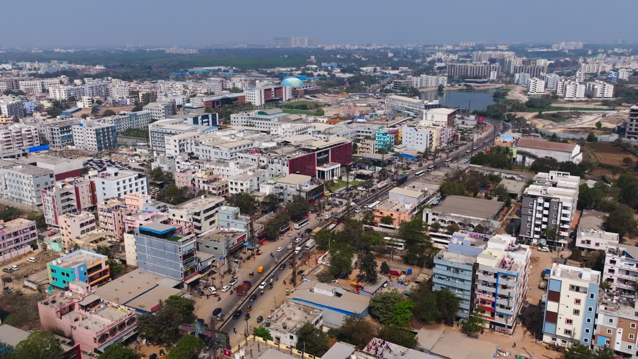 Traffico leggero su strada con edifici circostanti, lago e Malla Reddy Narayana Multispeciality Hospital a Suraram, Hyderabad, Telangana, India. Di giorno, ripresa con avvicinamento, ripresa con drone, 4K