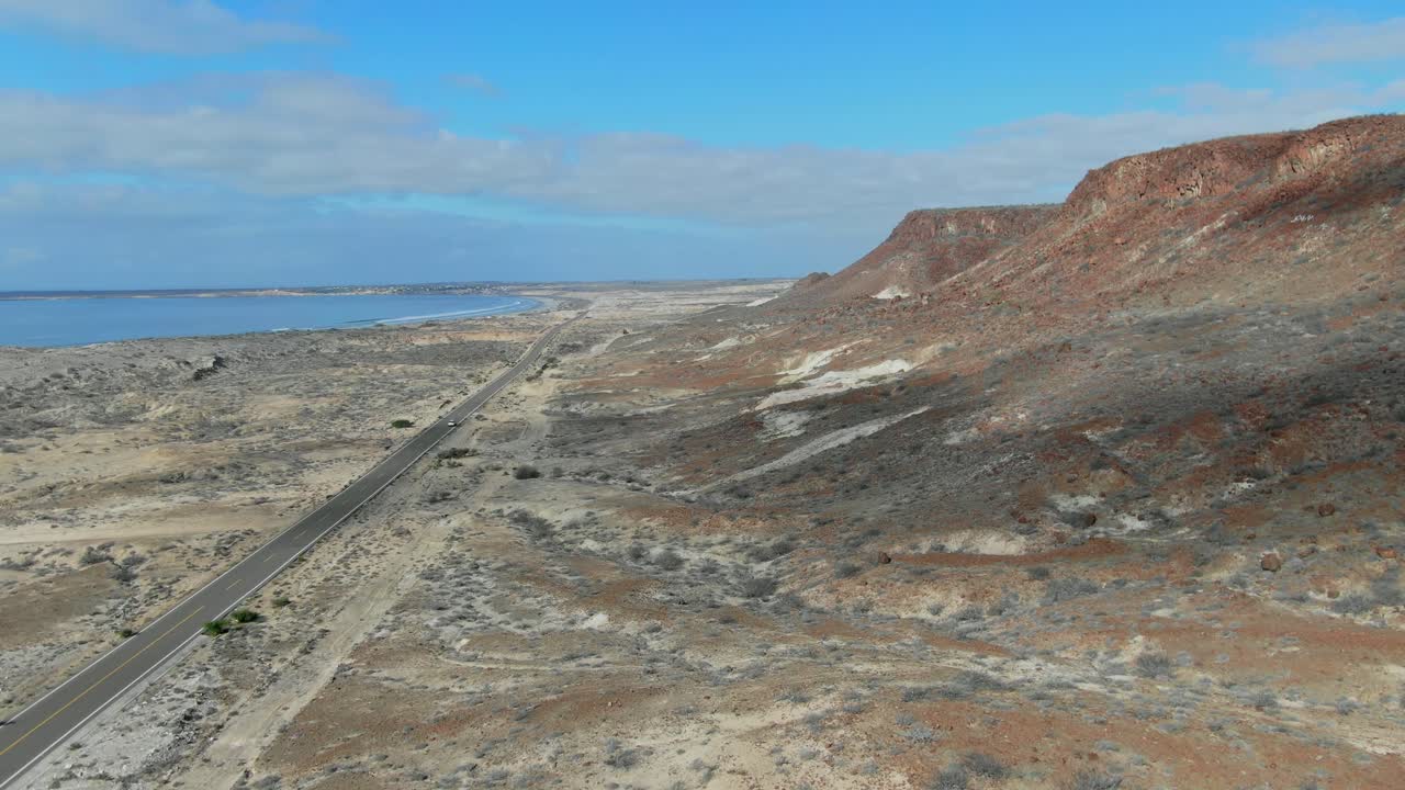 аэрофотосъемка движения вперед, живописный вид автомобиля, движущегося по шоссе у побережья ла пурисима баха калифорния сур, мексика, ярко-голубое небо на заднем плане