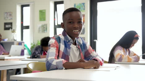 in school, smiling african american boy writing in notebook, feeling confident and focused