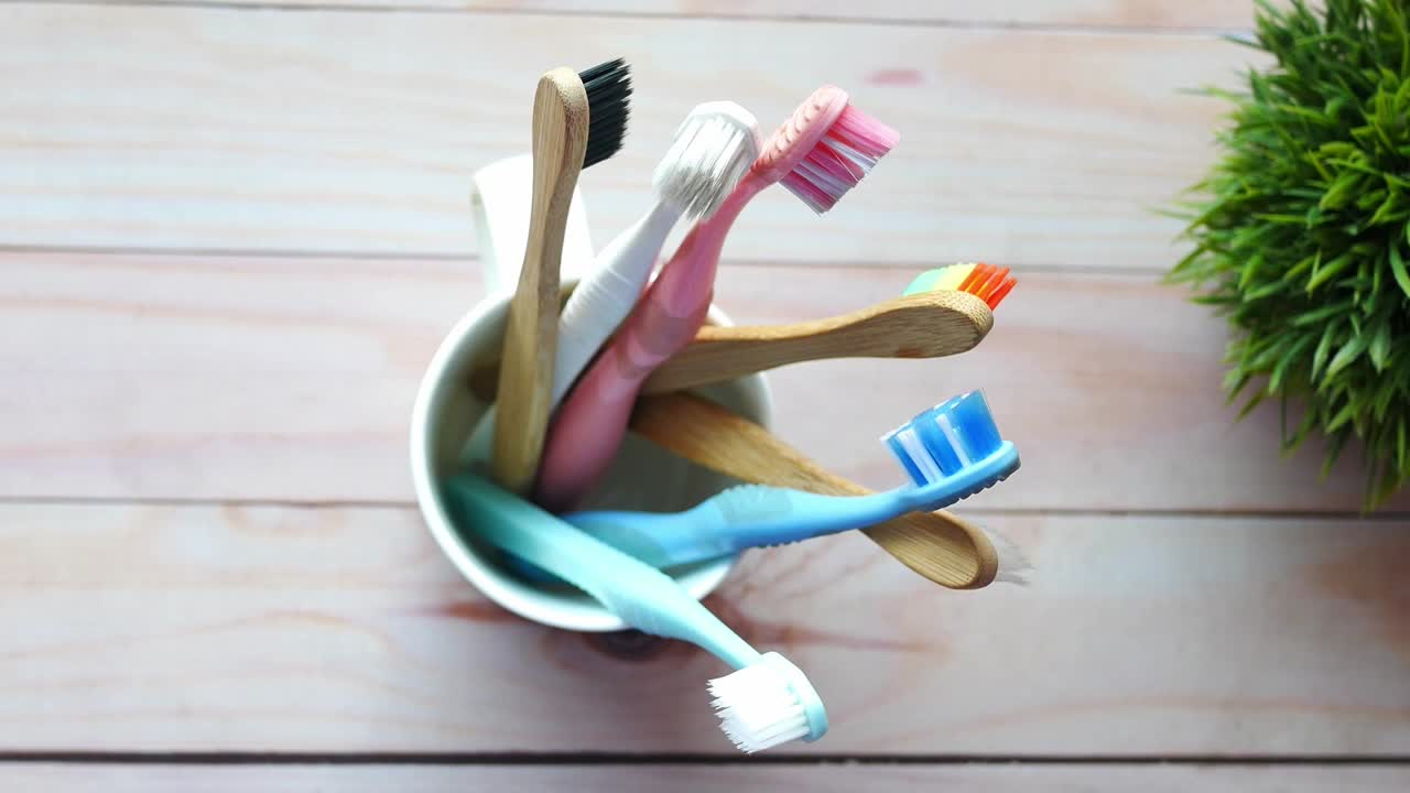 cepillos de dientes de diferentes colores en una taza en una superficie de madera ligera