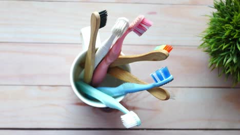 different colored toothbrushes in a cup on a light wooden surface