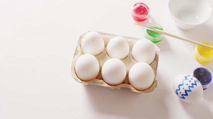 White eggs with colorful paints and brush on white background with copy space