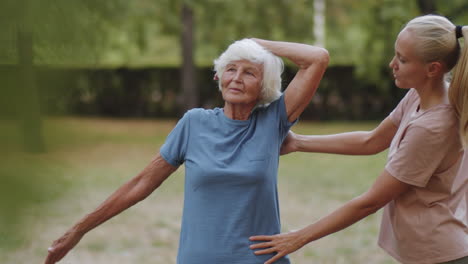 senior woman exercising in park with help of female trainer