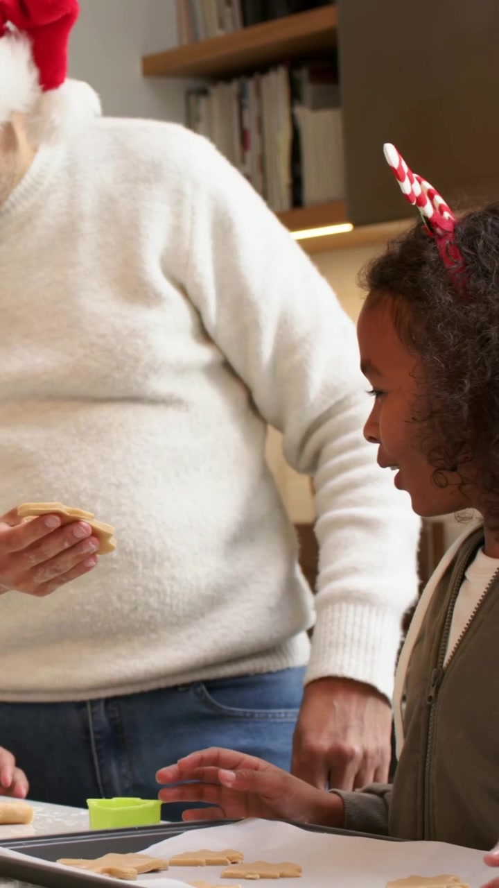 Video verticale: Applaudendo, papà con cappello di Babbo Natale che insegna al figlio a fare biscotti sul bancone con un tagliabiscotti verde.