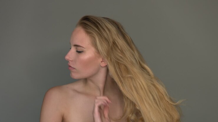 Donna sana si pettina i lunghi capelli biondi con le mani.