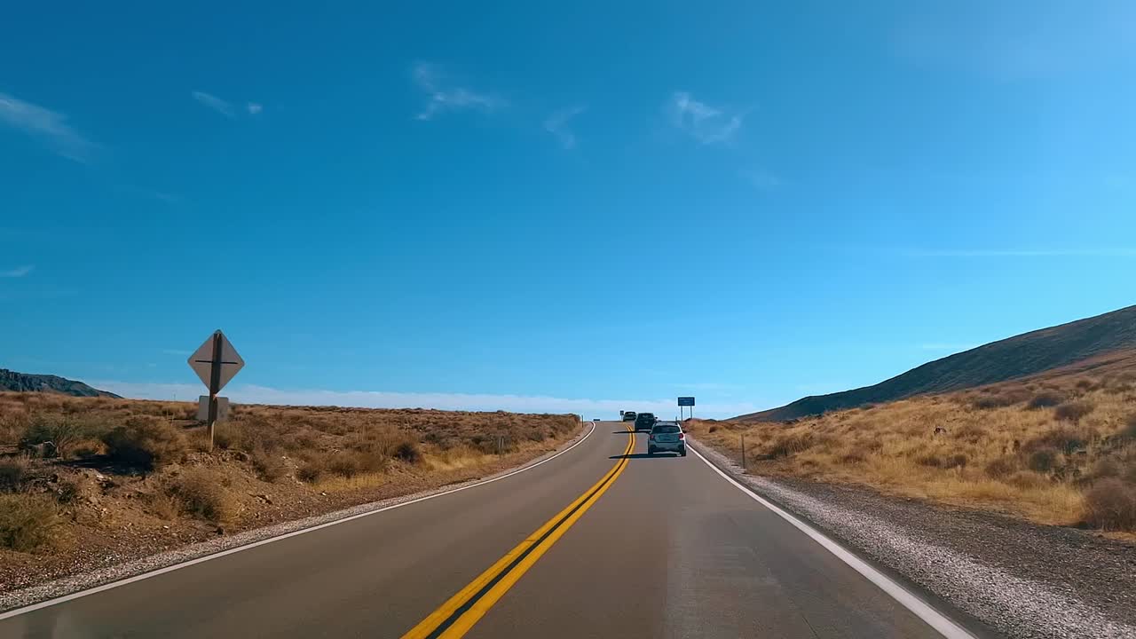Coche circulando por una carretera pavimentada a través de colinas áridas. Vehículo viajando por una autopista de asfalto a través de terreno montañoso seco bajo un cielo despejado.