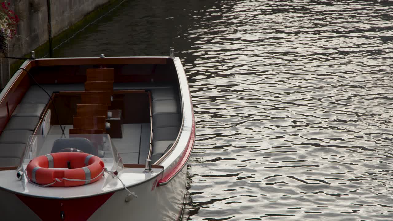 Empty canal boat drifts along calm water by stone wall in soft, tranquil evening light