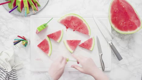 slicing red watermelon into small pieces on a white cutting board.