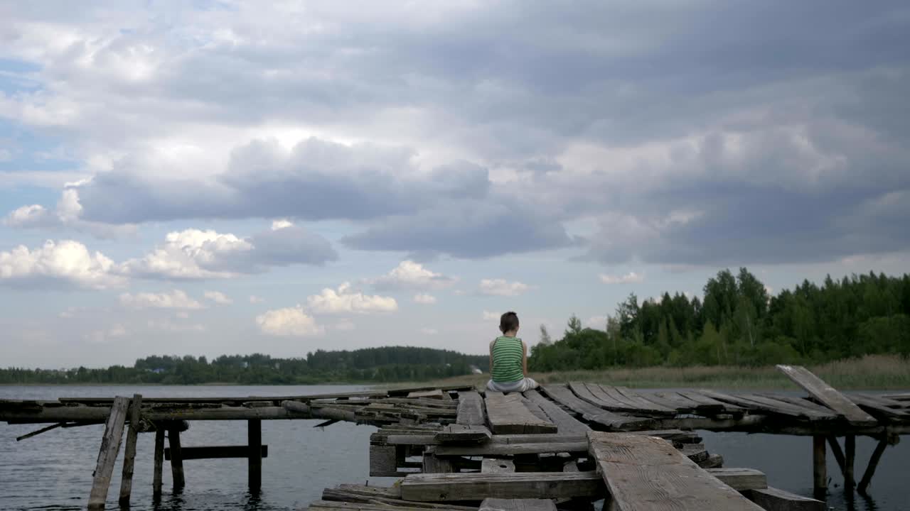 A lonely boy sits on the edge of the pier in windy rainy weather