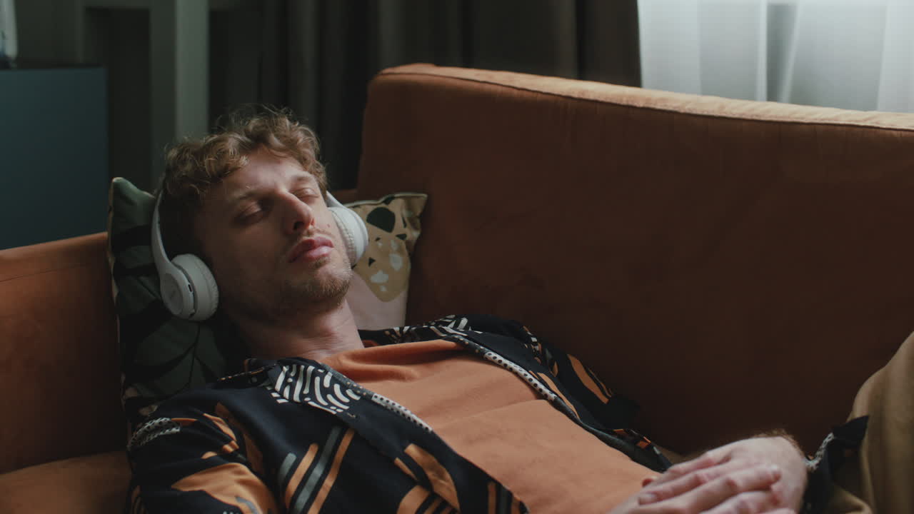 Relaxed Man Lying on Couch, Listening to Music with Headphones