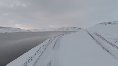Winding-snowy-road-by-oceanshore-and-girl-walking,-fast-dolly-forward-drone-view