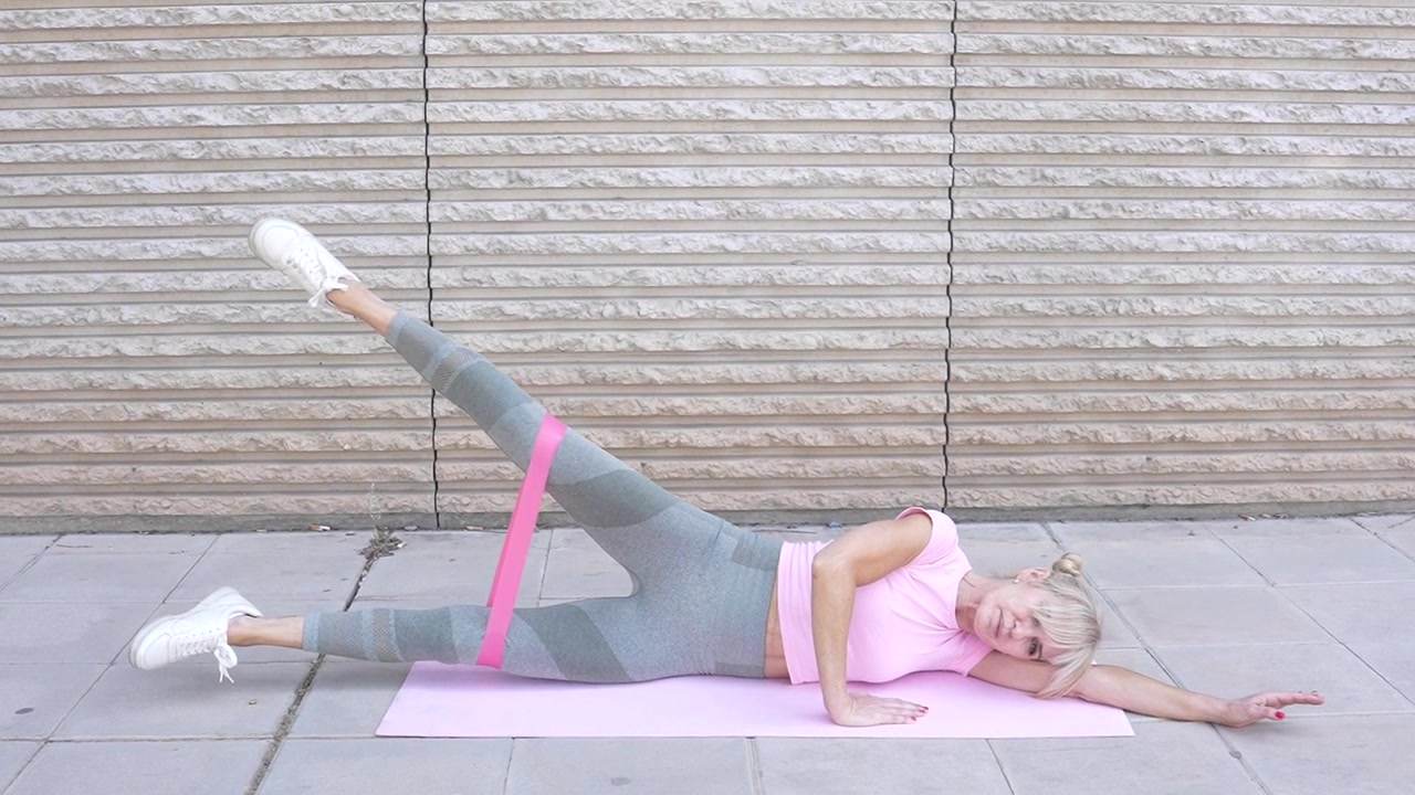 Woman demonstrates outdoor exercise with resistance band working on side leg raises sequence