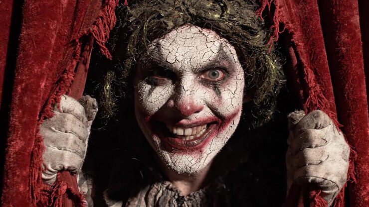 Un clown inquietante emerge da tende rosse strappate in un ambiente buio, catturando l'essenza della paura e dell'attesa in un'atmosfera di suspense