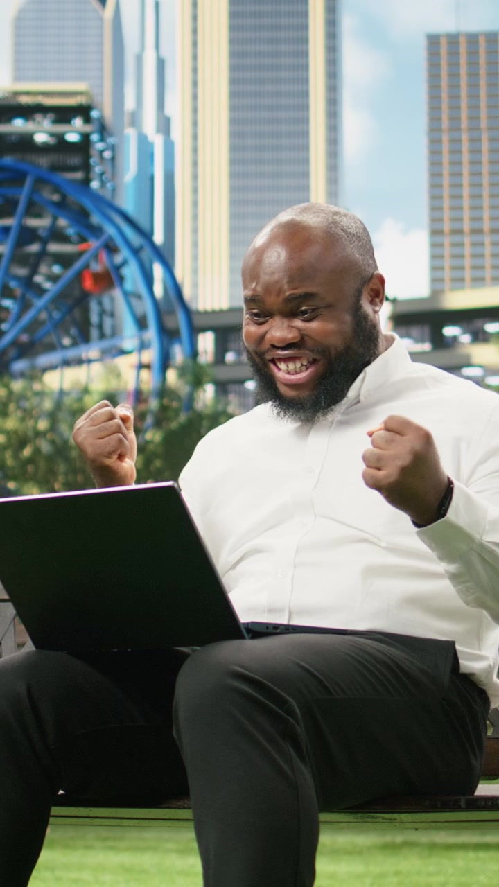 Vertical Video Excited businessman raising clenched fists while looking at laptop