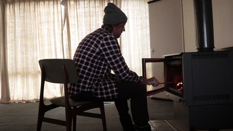 Un-Hombre-Con-Una-Camisa-De-Franela-Avivando-Un-Fuego-En-Una-Chimenea-Dentro-De-Una-Cabaña