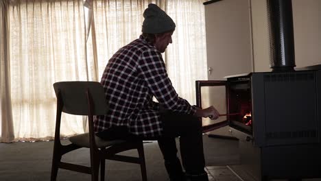 un hombre con una camisa de franela avivando un fuego en una chimenea dentro de una cabaña