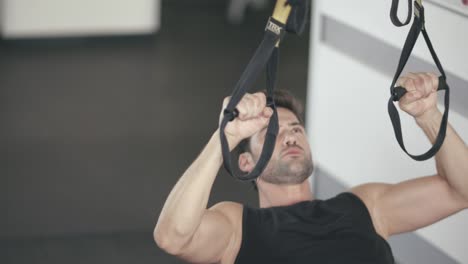 hombre atleta usando bucles de fitness para el ejercicio de pull ups en el gimnasio.