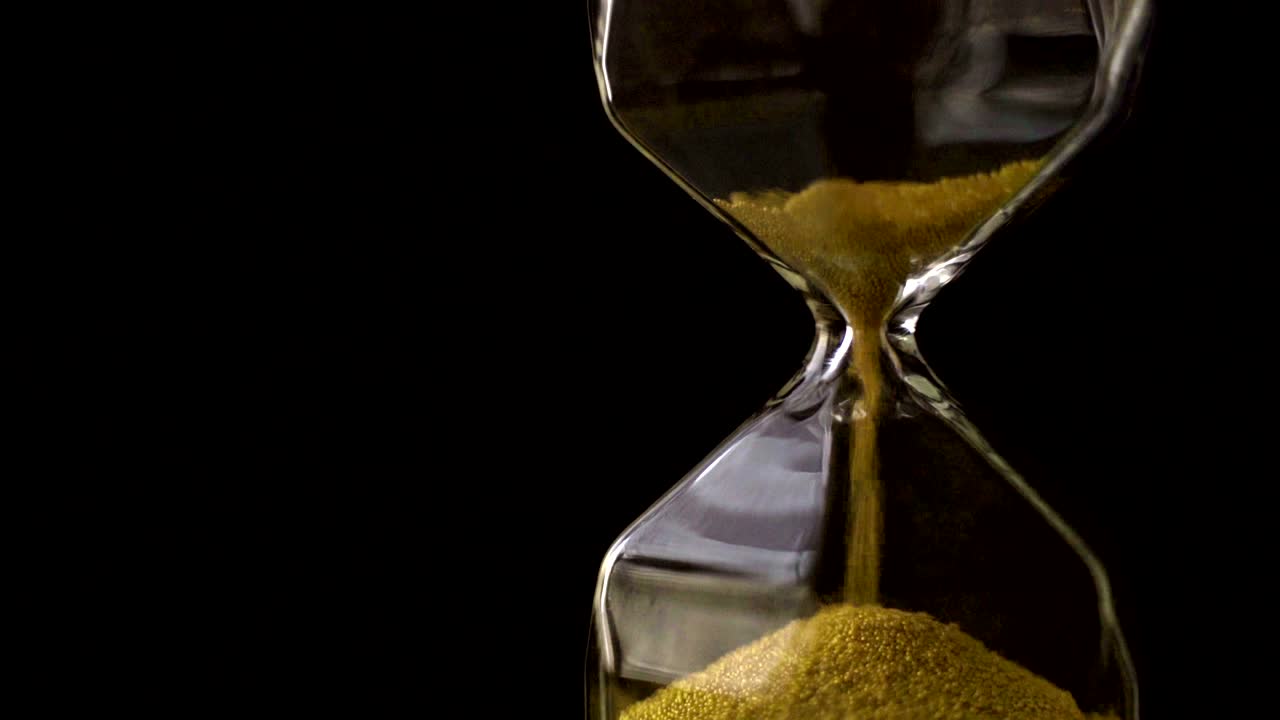 4k-slowmotion, der sandfluss in der sanduhr mit schwarzem hintergrund