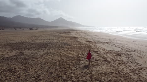 una mujer con un vestido rojo caminando sola en una playa soleada en fuerteventura
