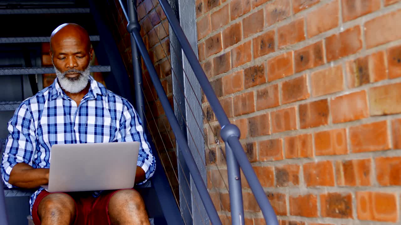 Senior man using laptop on stairs in living room 4k