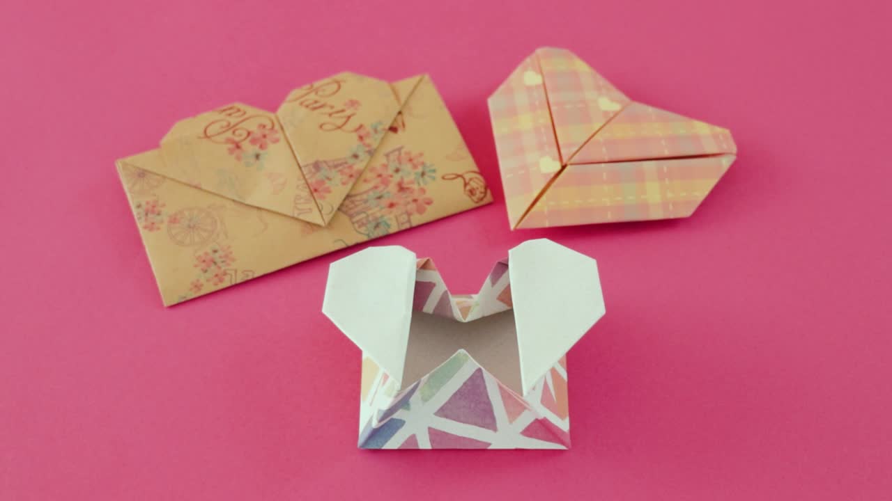 Heart-shaped envelopes folded from origami paper on pink tablecloth
