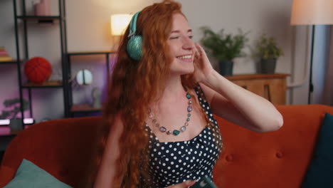 Happy-young-redhead-girl-in-wireless-headphones-dancing-singing-listening-favorite-song-at-home-room