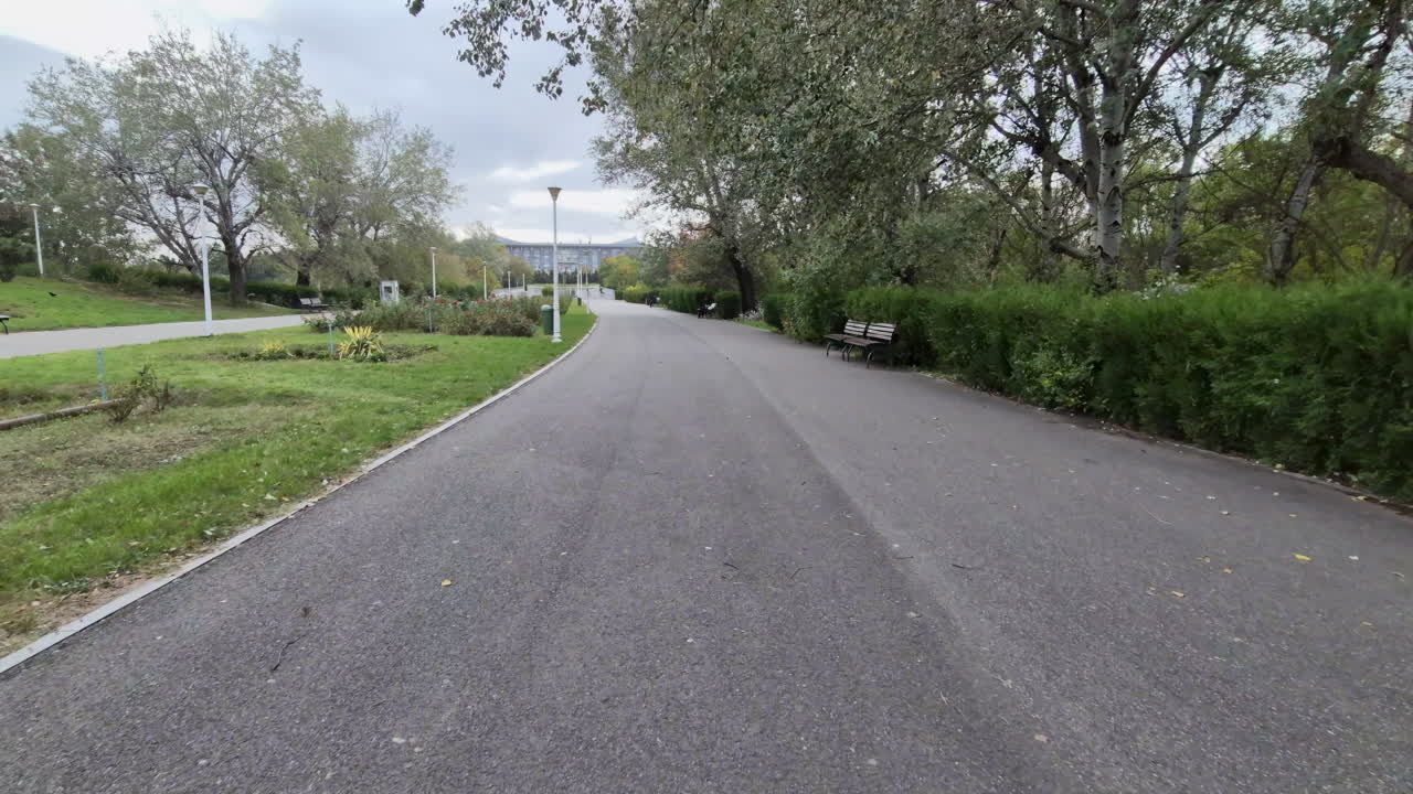 Wide view of an empty park path lined with benches and green trees on an overcast autumn day