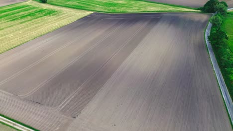 aerial-shot-of-plowed-farmland-and-green-fields,-4k