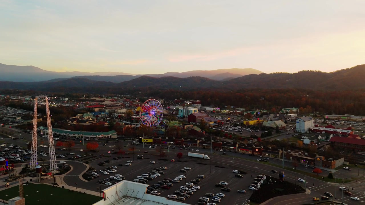 Uma tomada de drone em 4K na hora dourada, recuando sobre Pigeon Forge, Tennessee, durante o pôr do sol. A vista ampla destaca a roda-gigante ao longe, emoldurada por uma paisagem cênica
