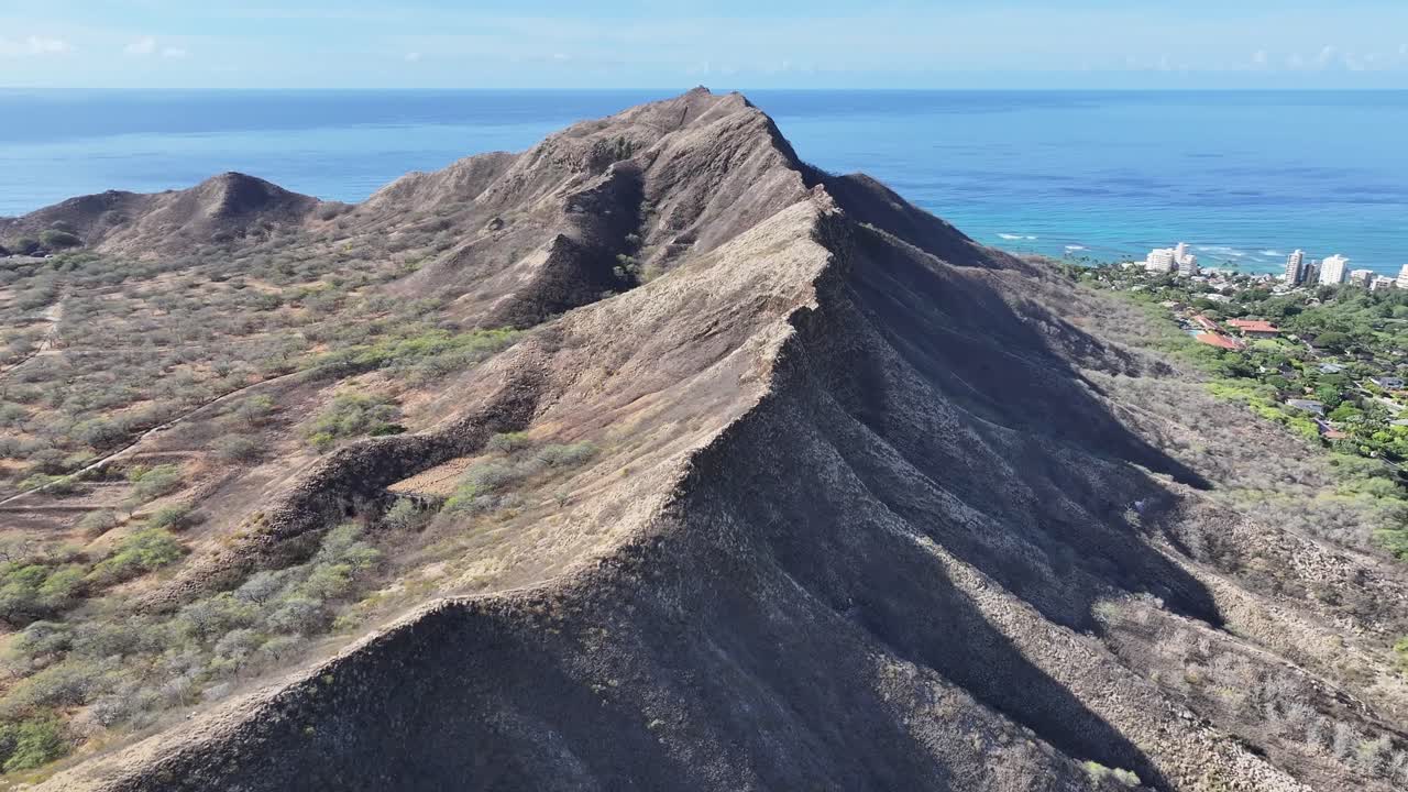 Aerial drone footage along the rim of Diamond Head volcanic crater on Oahu, Hawaii, showcasing panoramic tropical landscapes, turquoise ocean views, palm trees, and the scenic Waikiki coastline below