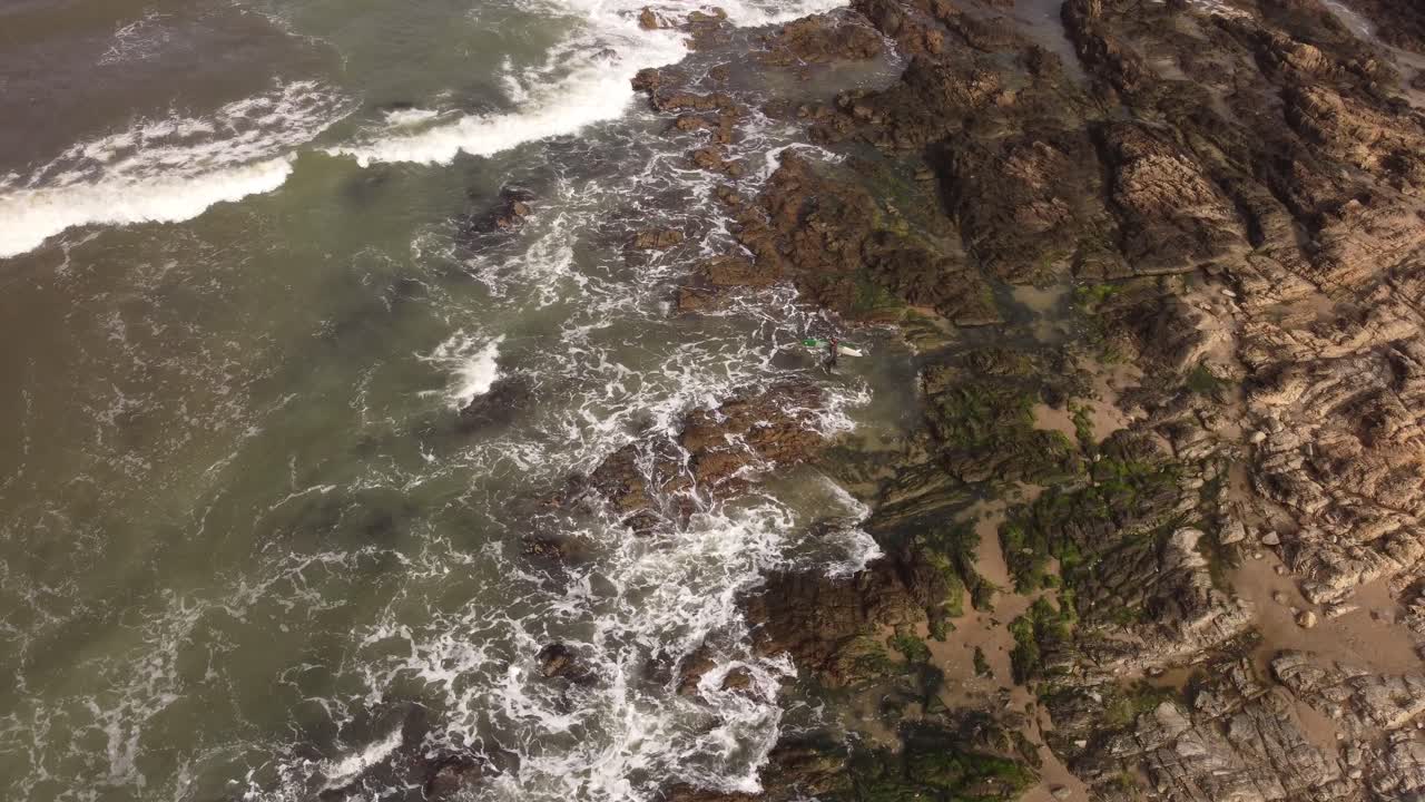 alto vuelo de drones sobre un surfista que ingresa a los mares agitados del océano atlántico cerca de las costas rocosas de punta del este en uruguay