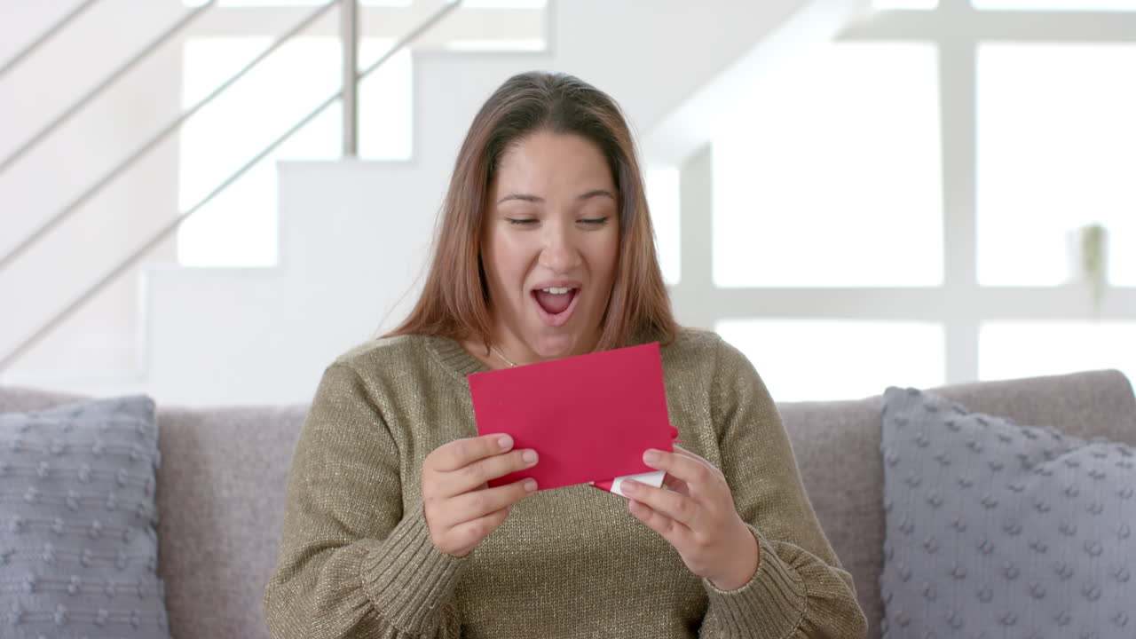 Glad kvinde i stor størrelse af blandet etnisk baggrund har videoopkald i stuen med kort og gave, slowmotion