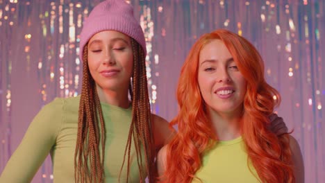 studio portrait shot of two young gen z women standing in front of tinsel curtain against pink background 2