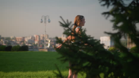 joven patinando al aire libre en un parque soleado, balanceando sus manos abiertas para el equilibrio, con una vista borrosa del paisaje urbano y los rascacielos, el fondo con vegetación exuberante, postes de lámparas y árboles