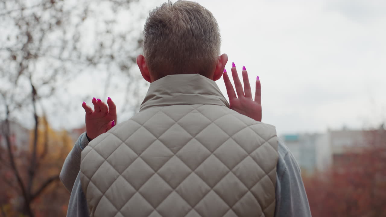 Siblings approach each other and share warm hug in urban park as autumn leaves sway gently in wind with painted nails visible and soft breeze moving branches